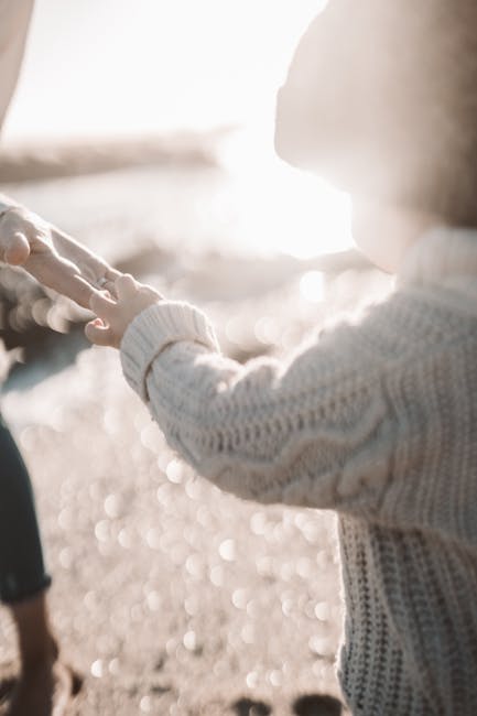 Child in knitted sweater holding hands by the beach, capturing a tender moment in natural light.
